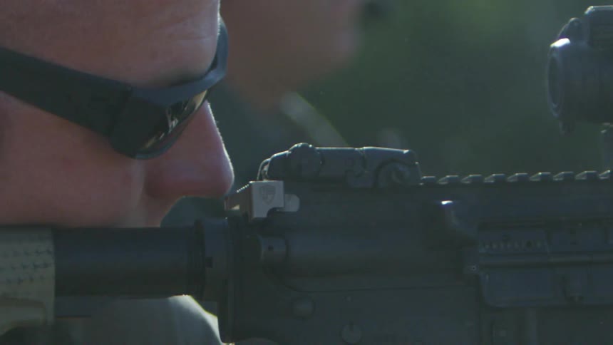 A white man fires an assault rifle outdoors