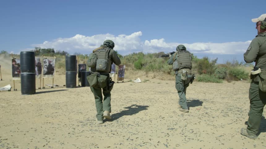 Two military police walk towards shooting targets with their guns while another watches them