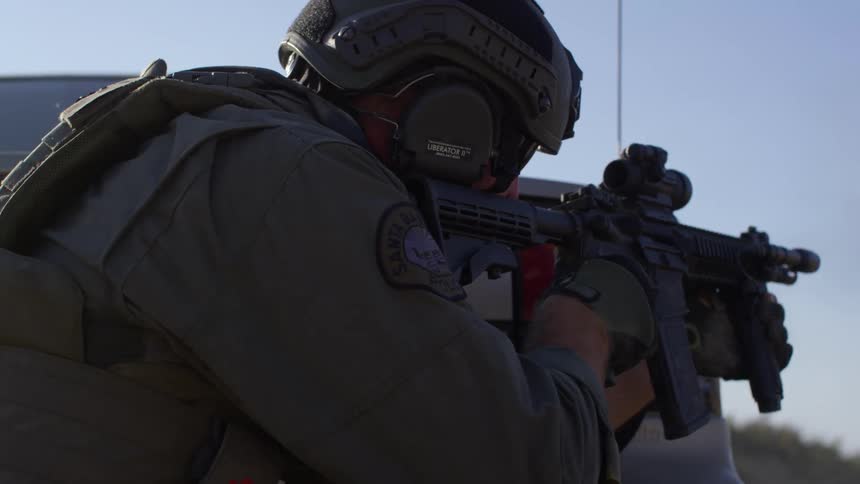 A military police ducks behind a car as she shoots his gun
