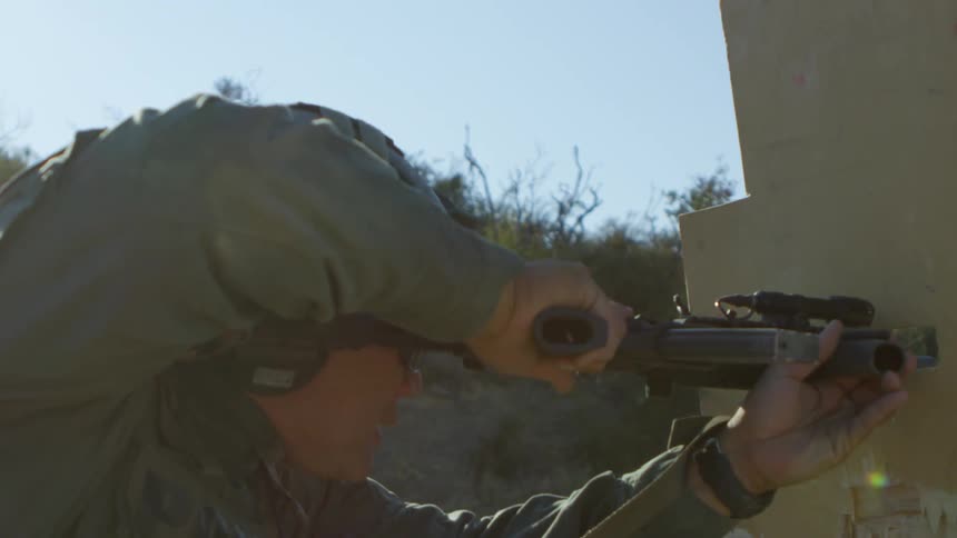 A policeman holds his gun as he hides behind a wall