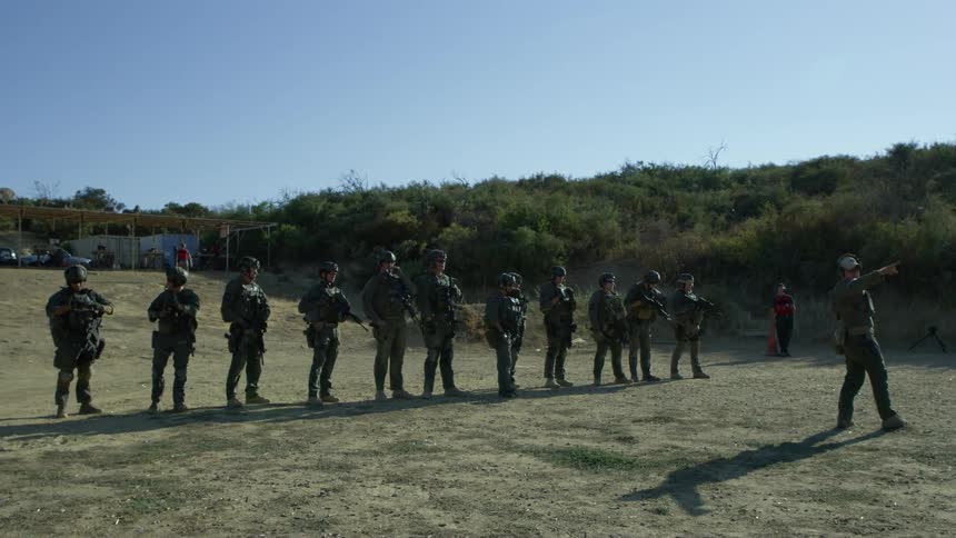 Instructor directs armored troops standing in line near hill