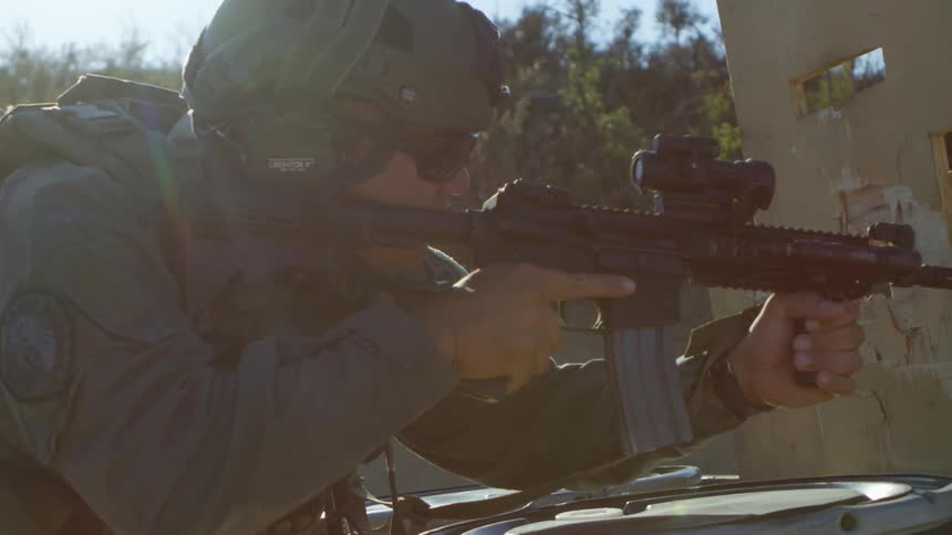 A soldier crouches and aims his gun