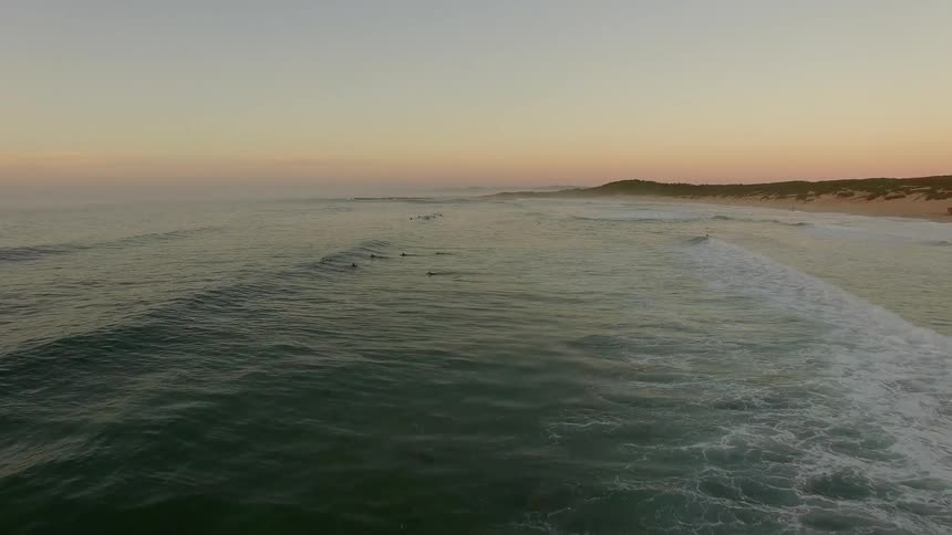 Surfers paddling out to sea at sunset