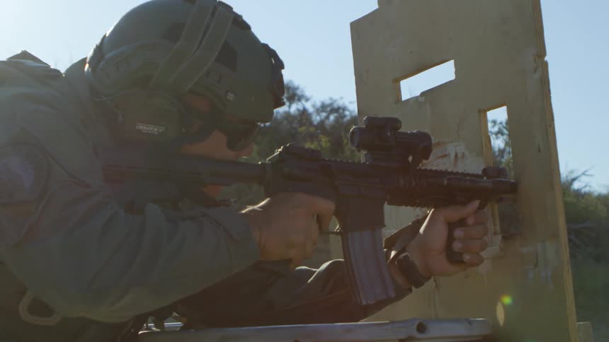 A man with a uniform helmet sunglasses and earmuffs shooting a rifle