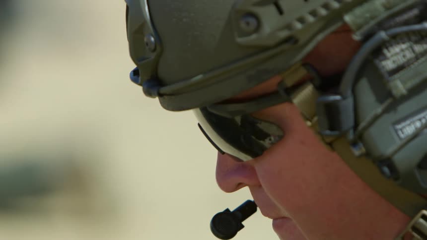 Military soldier wearing a helmet and sunglasses looks down as he adjusts something