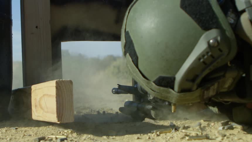 Dirt flies up as a police officer fires at a target while pressed to the ground