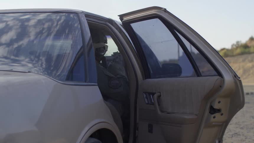 A soldier sits in a car and shoots at targets out the window