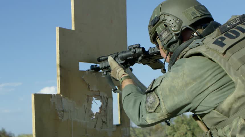 A military police ducks behind a board and aims his gun and fires