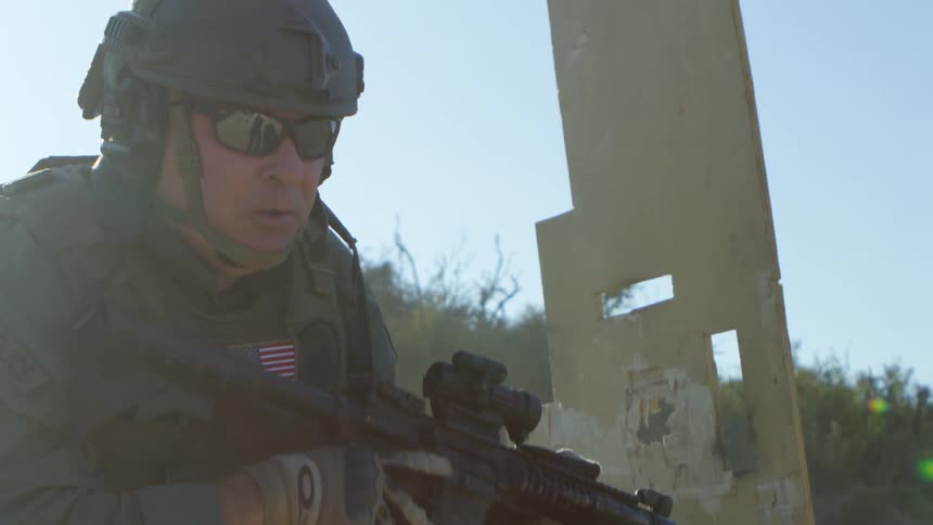 A man with a helmet headset and sunglasses shooting a rifle then running