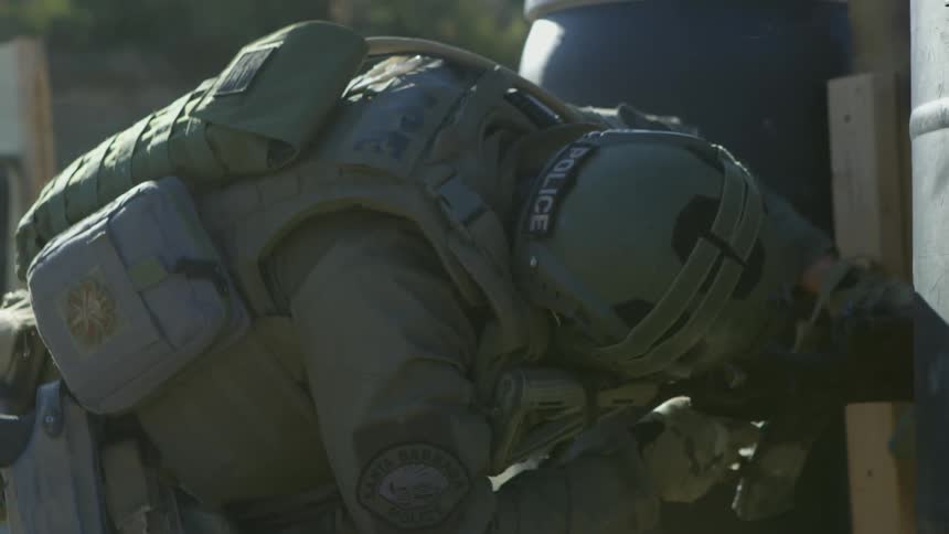 Soldier bends down to shoot rifle through narrow gap