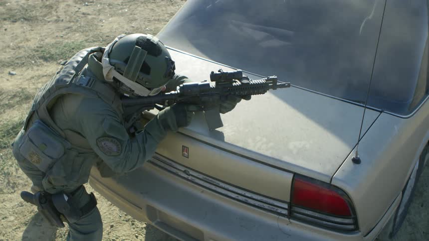 A police officer takes cover behind a vehicle as he fires shots from a machine gun