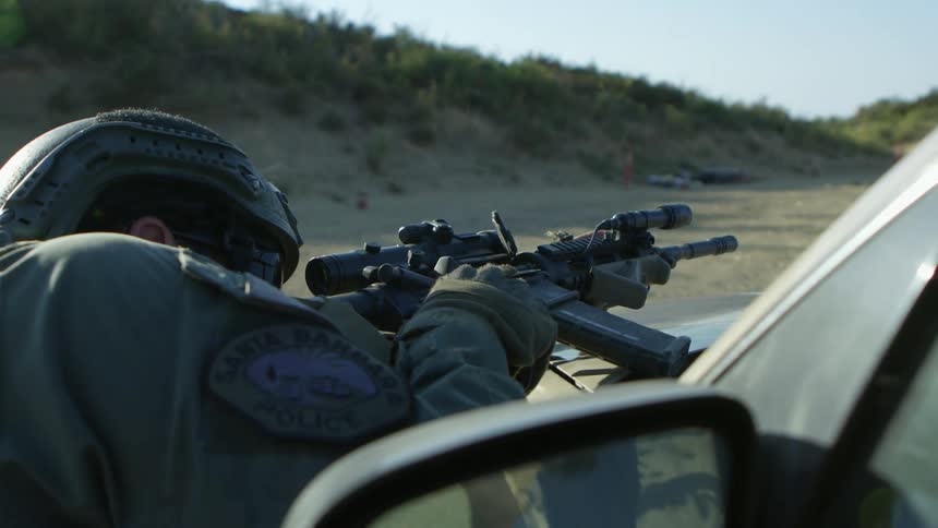 A military policeman stands behind a car and fires his gun