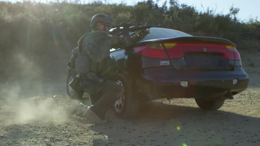 A military police runs and takes cover behind a car and fires his rifle