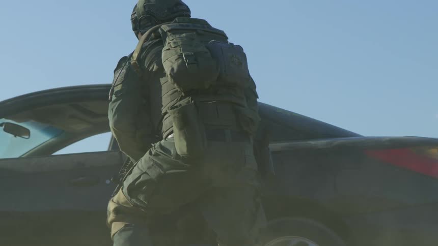 A soldier looks under the car and moves around with his rifle