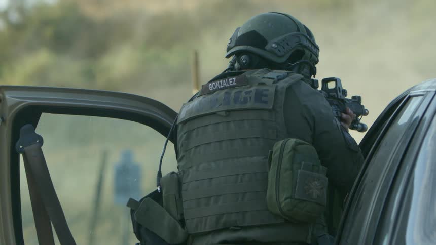 A soldier stands behind a car door and shoots a gun