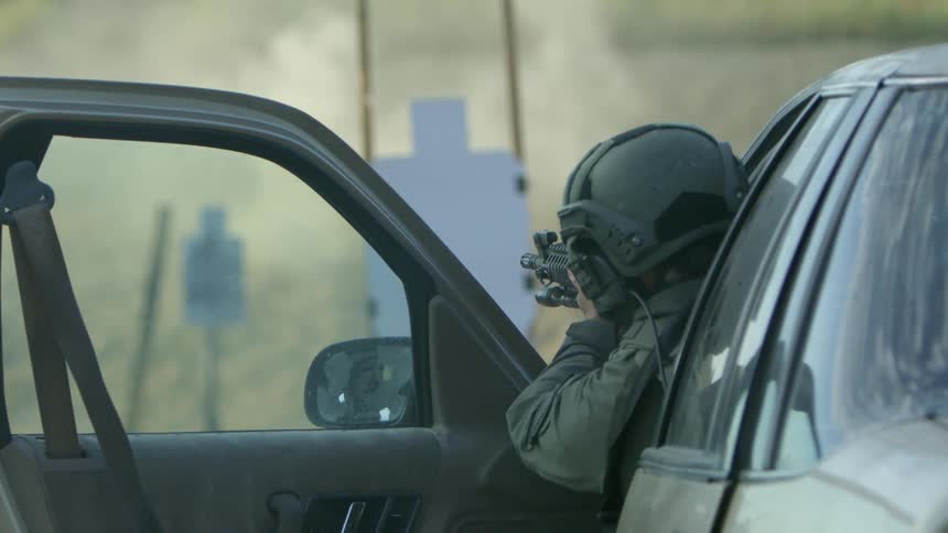A military police opens a car door and aims his gun at a paper target