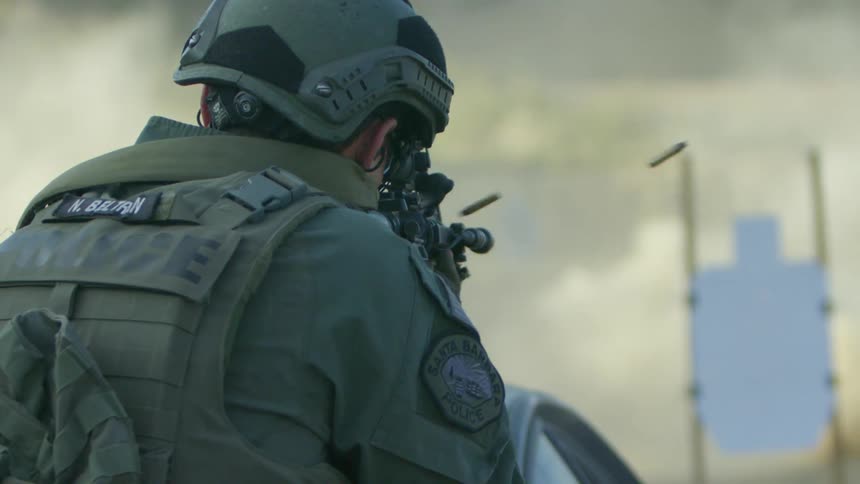 Police officer in military gear shoots assault rifle at a target