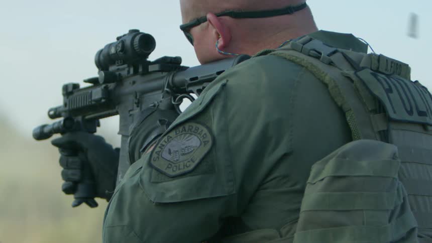 A man is firing his rifle by the vehicle