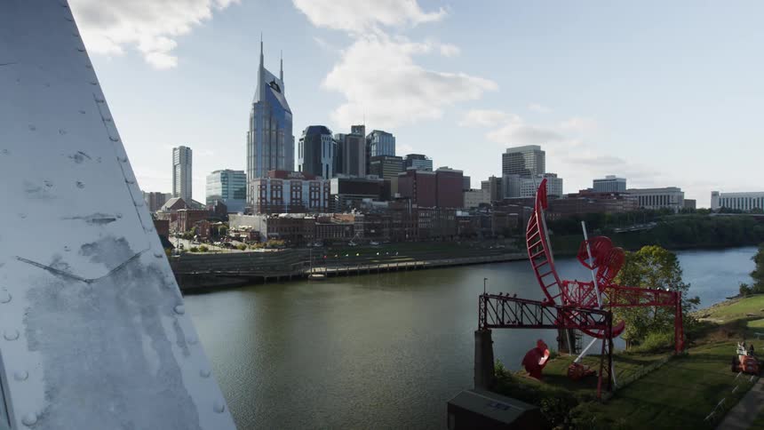 River sits with city buildings on one side and a park on the other under a sunny sky