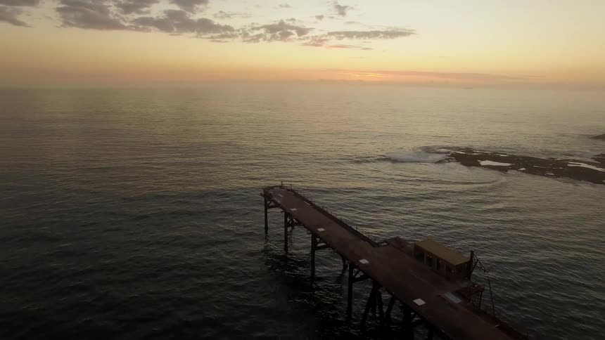 Aerial view of ocean waves flowing under and around a pier at sunset