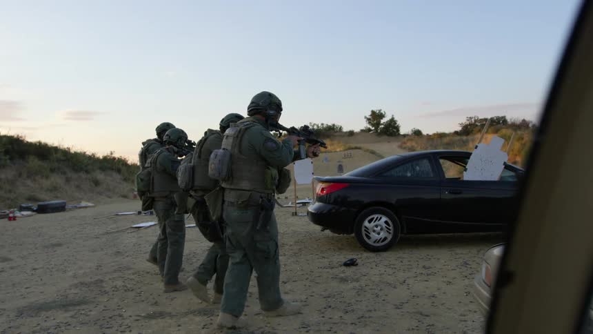 Three soldiers point rifles as they walk towards the car