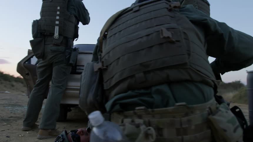 Two soldiers stand with weapons drawn while another soldier cares for a wounded man