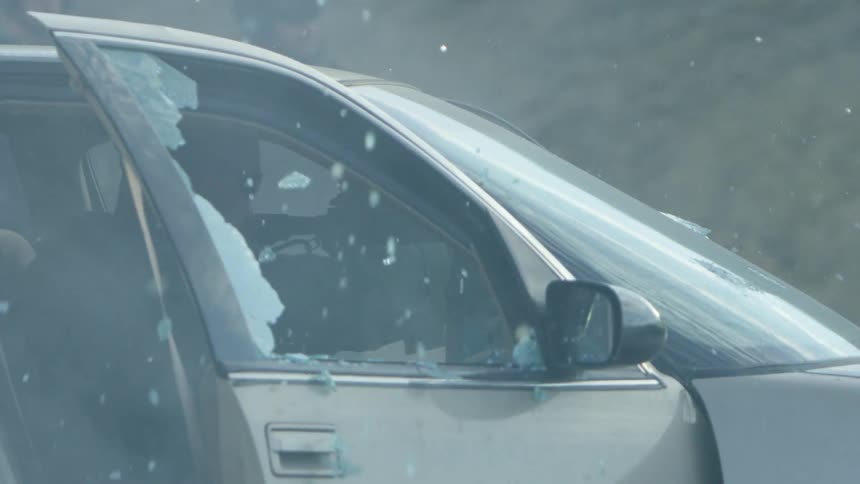 As a man sits in his car the passenger window is shot out