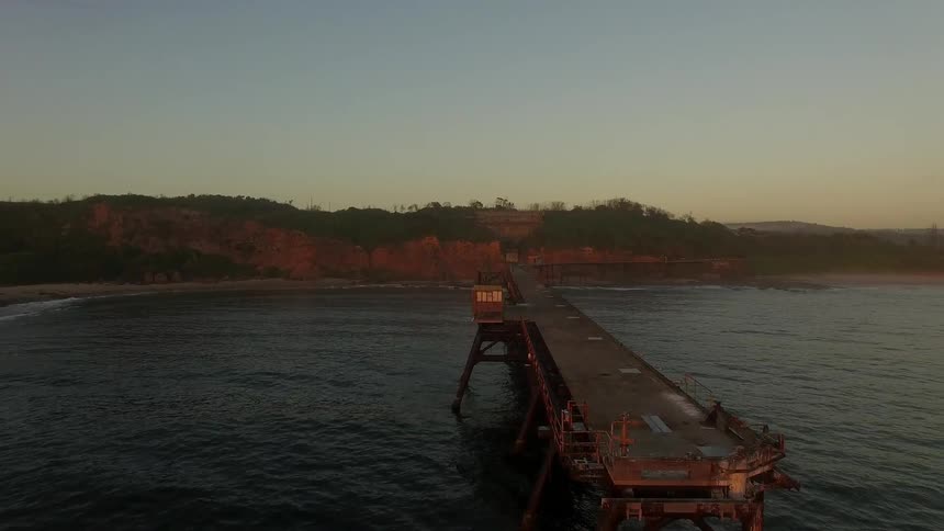 The sun is setting on a wooden pier going into the water