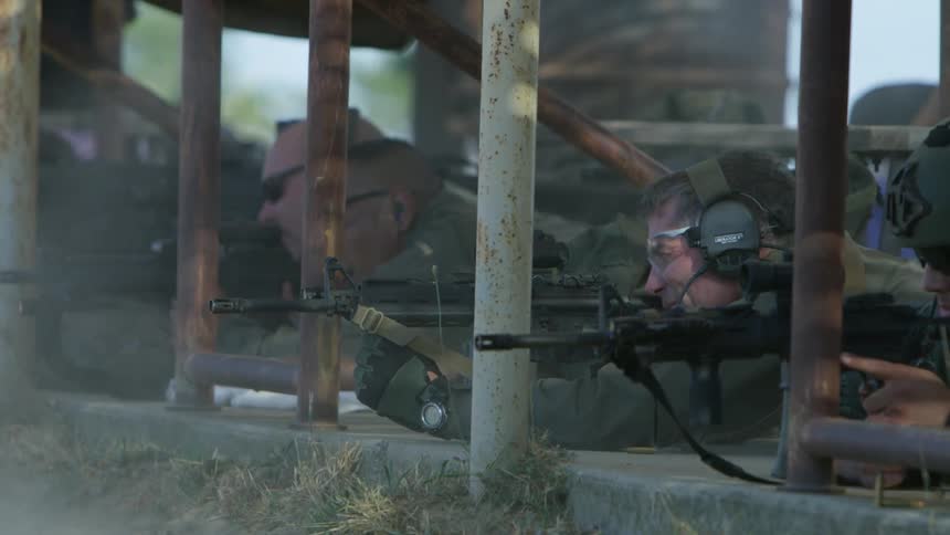 Police officers in military uniforms shoot assault weapons while laying on the ground
