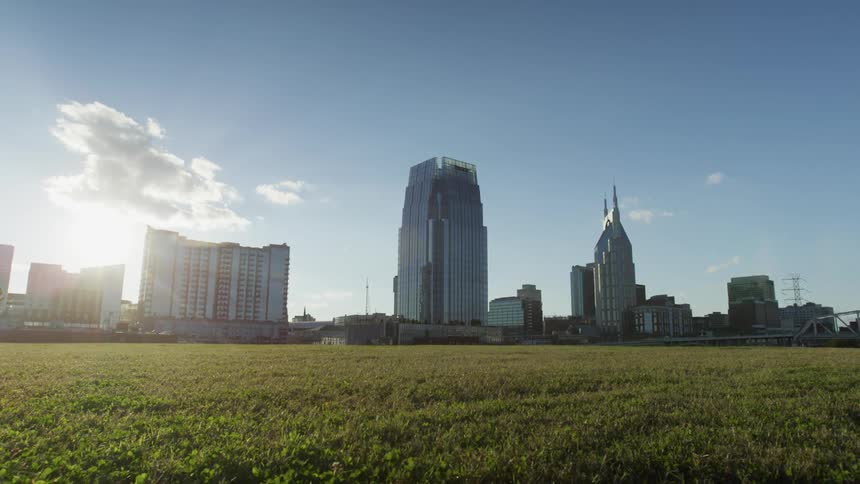 Sun brightens cloud hovering over mid rise buildings near wide grassy field