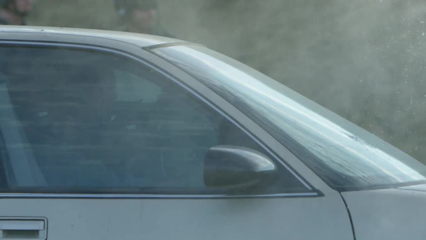 Two police sit inside a car and shoot out the front windshield as another police stands next to the car and watches
