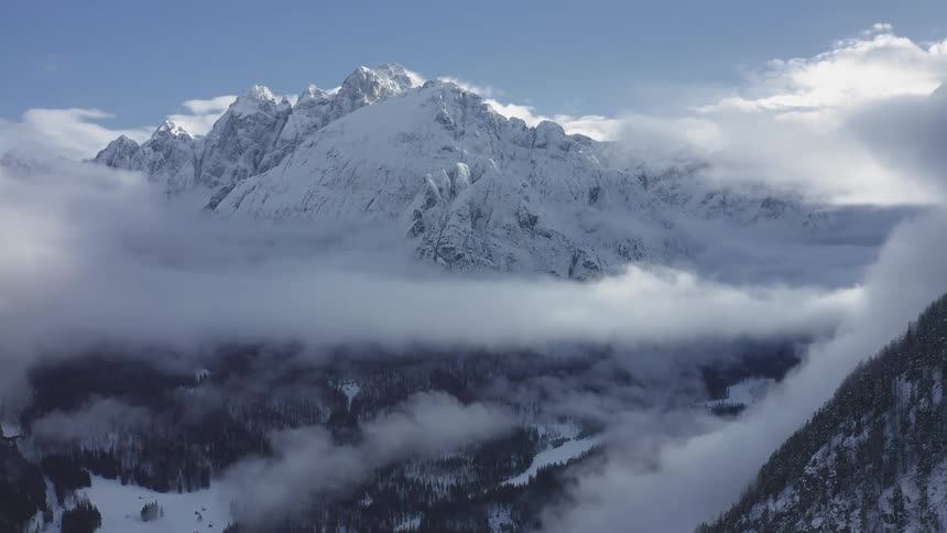 Aerial of snow covered mountain peaks surrounded by clouds