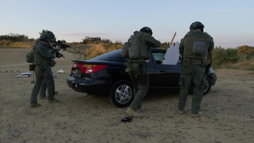 A small group of armed military approach a deserted vehicle
