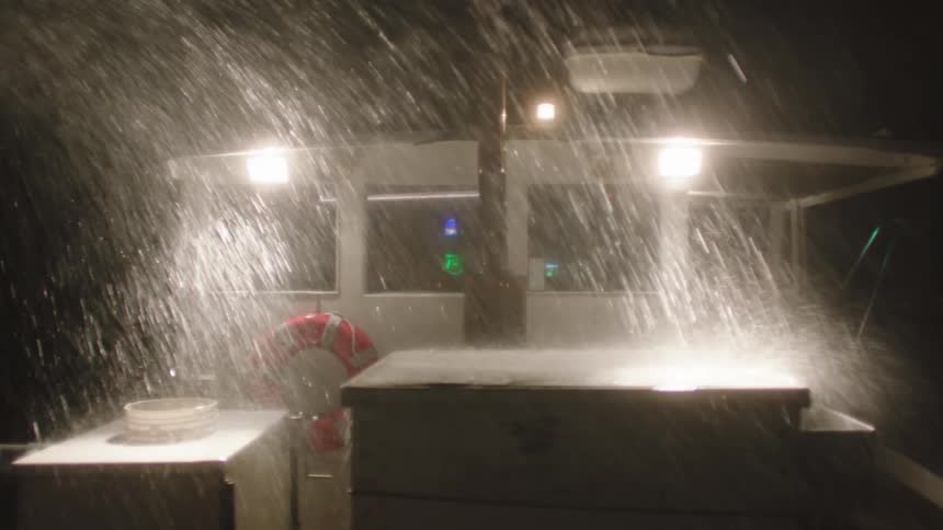 Water showers onto boat cabin and deck under glaring boat lights