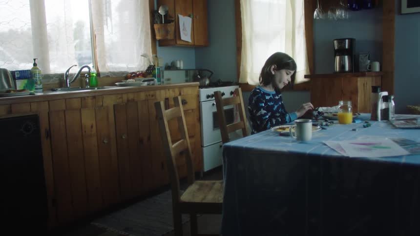A young girl sits at a kitchen table playing with a small toy