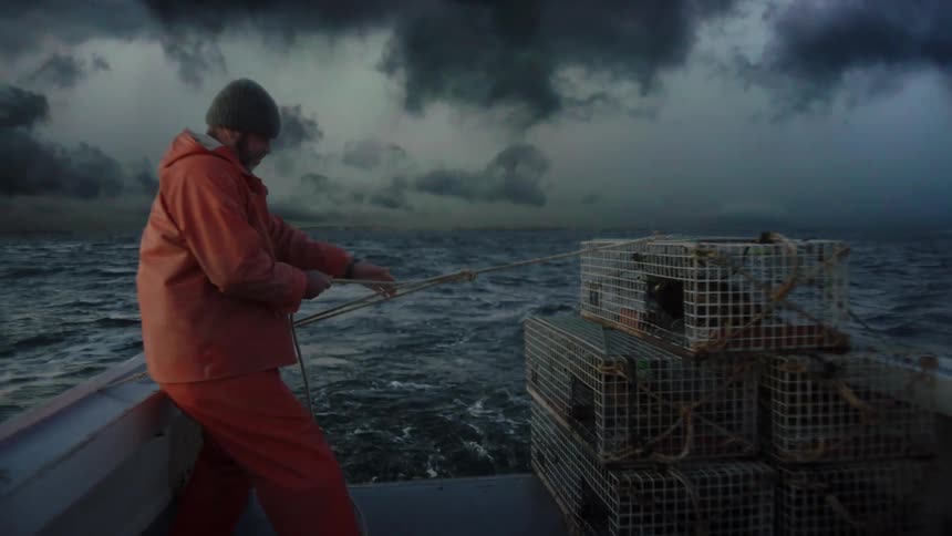 A man on a boat pulls a rope hard to secure crates during a storm
