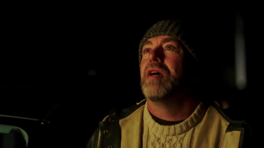 Man with a beard and beanie gets out of a car and looks up at the light smiling slightly at night