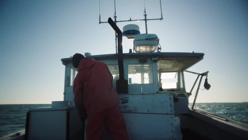 A man on a boat takes a lid off of a big box