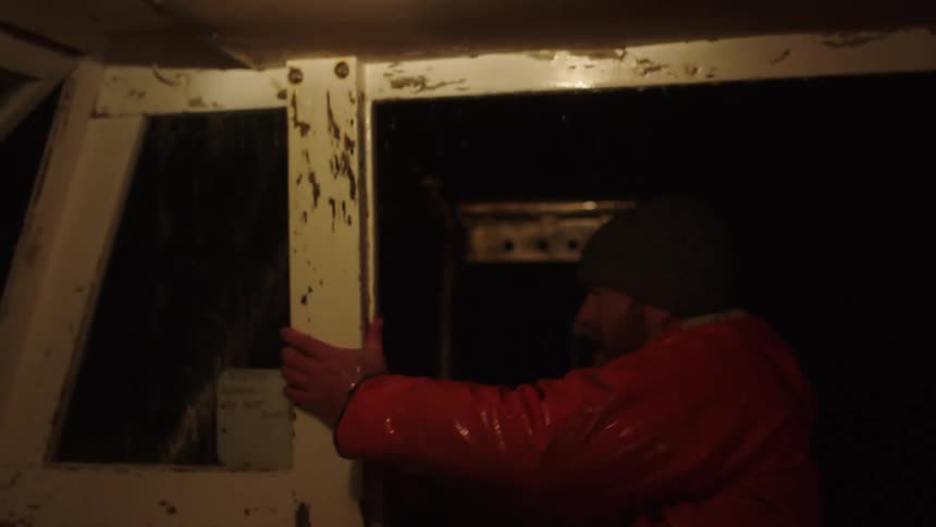 Boat pilot stares out of the cabin during a storn at night