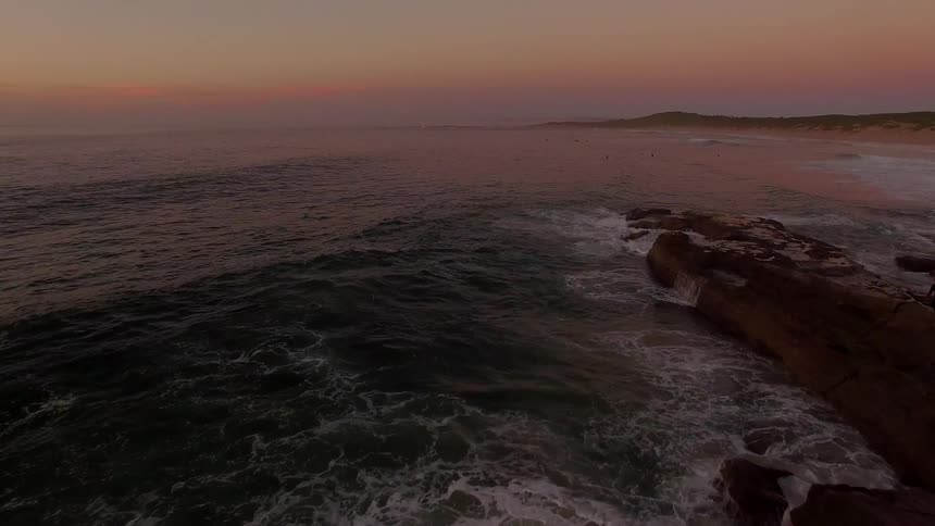 The sun is setting over the ocean as waves crash on the shore