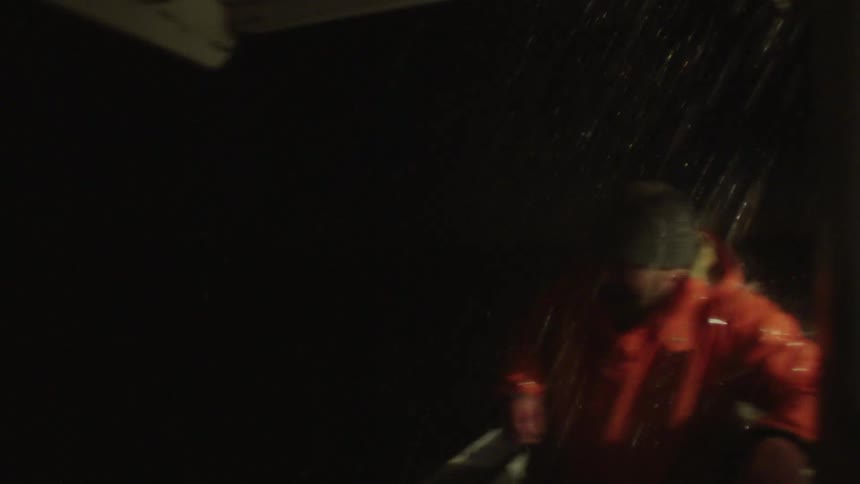 A man with a hat and orange raincoat getting wet by water