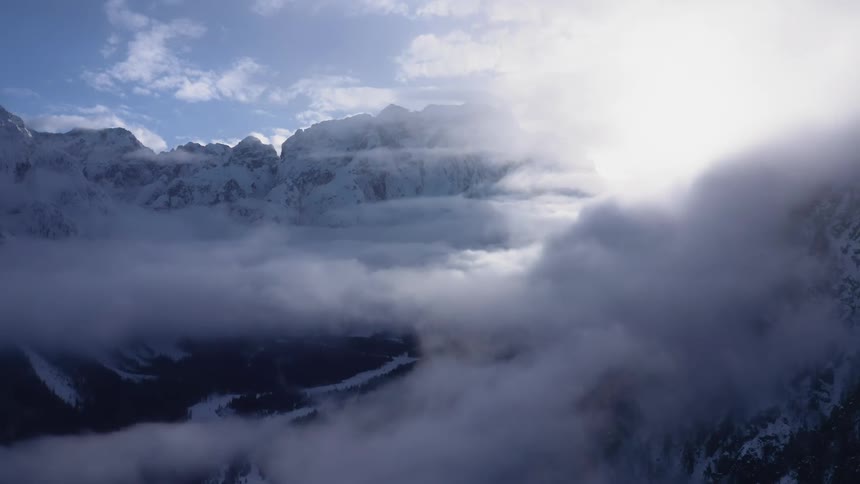 Snow capped mountains shrouded in cloud and fog on a sunny day
