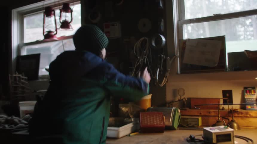 Male child runs into a workshop and climbs up on the work bench to remove duct tape from the hook on the peg board and climbs back down