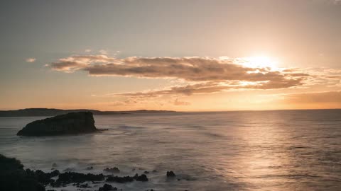 Time-lapse of waves washing against rocks as clouds drift in front of the setting sun