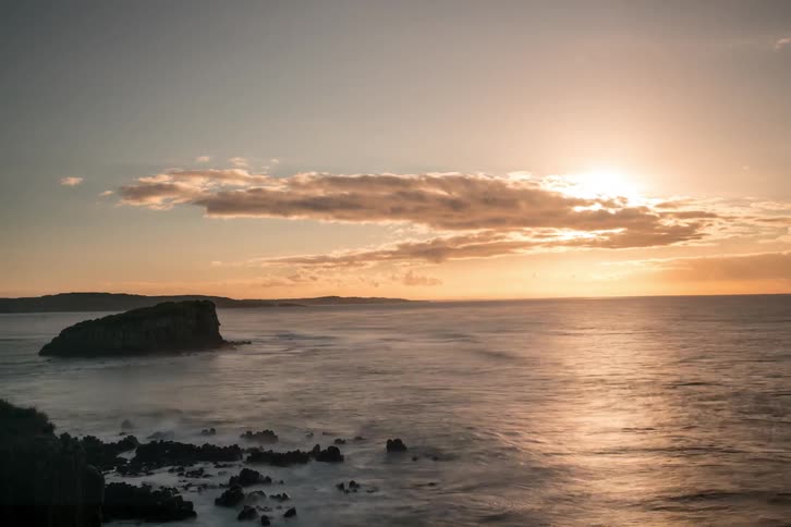 Time-lapse of waves washing against rocks as clouds drift in front of the setting sun