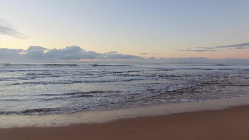 An empty beach has waves crashing on the shore at sunset