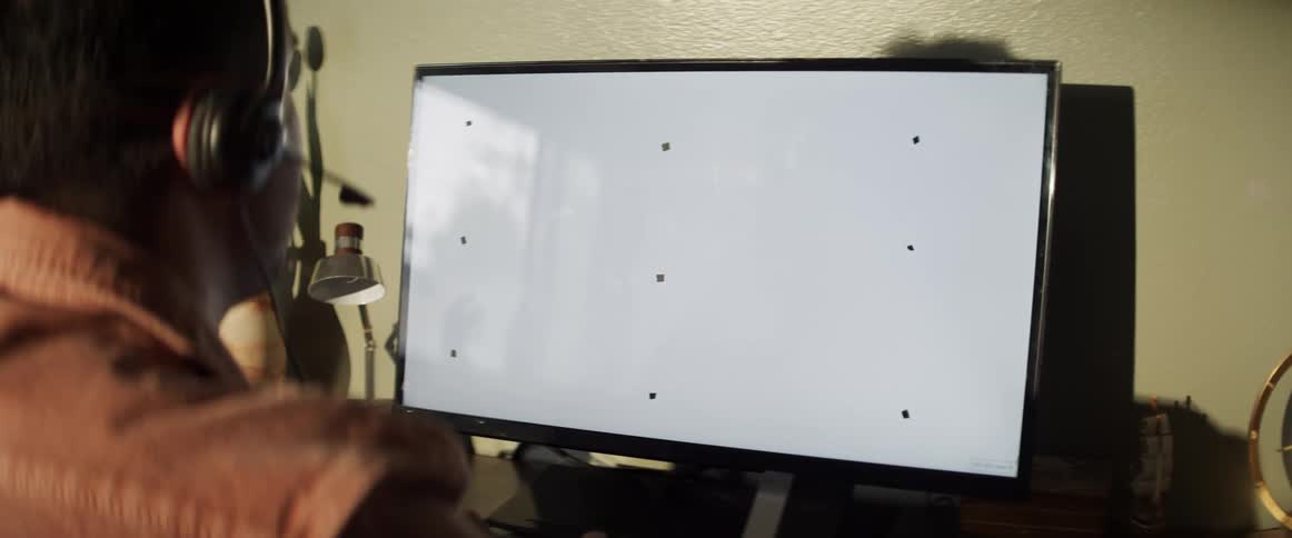 A man sits in his office and looks at a computer screen while talking on a headset