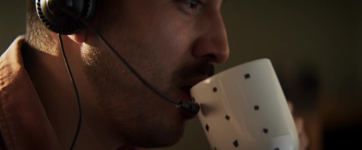 A man talking in to a head set drinks out of a mug