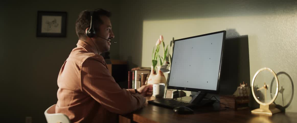 Man drinks from coffee cup while listening to computer via headphones