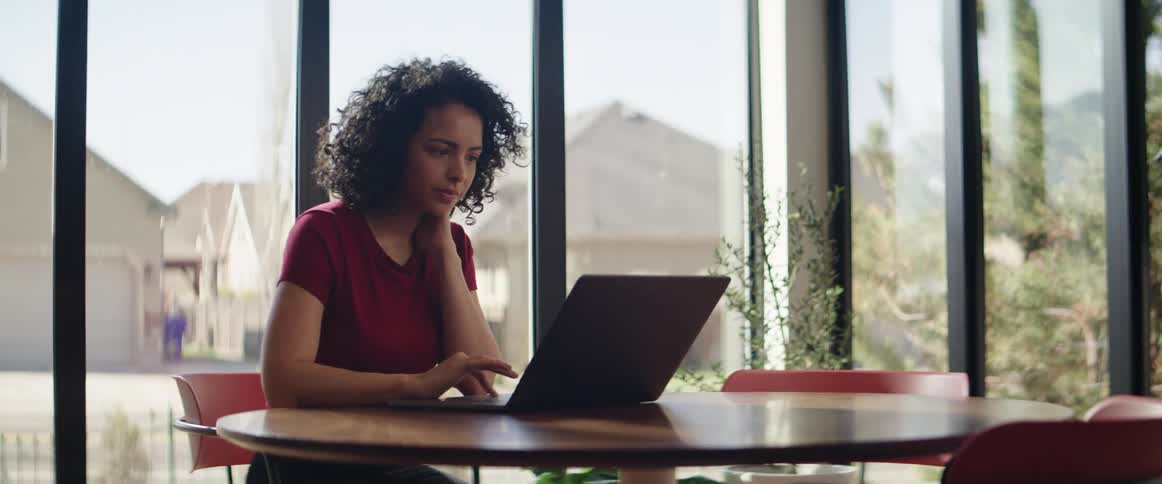 A teenager sits at a table and works on her laptop